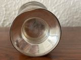 a silver cup sitting on a wooden table with a white wall behind it