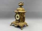 a gold clock sitting on a stand with a bird on top