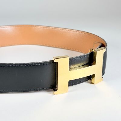 ceinture en cuir noir avec une boucle en H dorée sur fond blanc