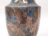 un vase bleu et brun posé sur une surface blanche