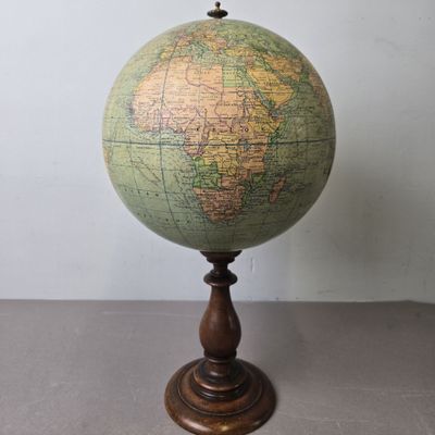 un vieux globe terrestre posé sur un socle en bois, avec un mur blanc en arrière-plan