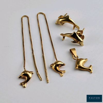 trois colliers en or et une paire de boucles d'oreilles posés sur une surface blanche