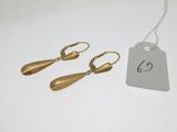 deux paires de boucles d'oreilles en or, accompagnées d'une étiquette de prix, posées sur une table blanche