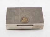 an antique silver cigarette case with a coin on top