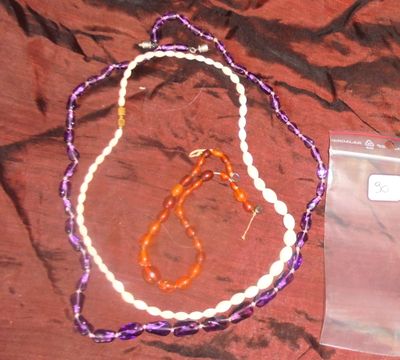 des colliers de perles violettes et blanches et un sac en plastique posés sur un lit