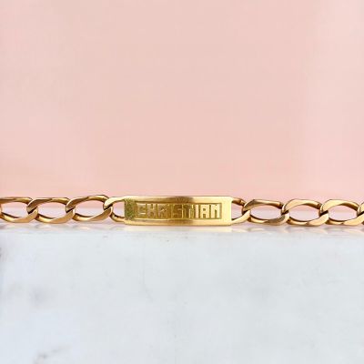un gros plan sur un bracelet à chaîne en or orné d'une plaque portant un nom