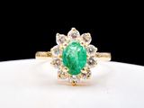 a close up of a green emerald and diamond ring on a white plate