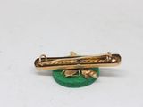 a close up of a gold plated tie bar on a green base