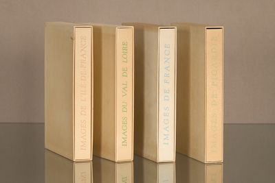 Trois livres sont alignés sur une table dont la surface produit un reflet.