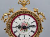 a gold clock with a red and white face on a stand