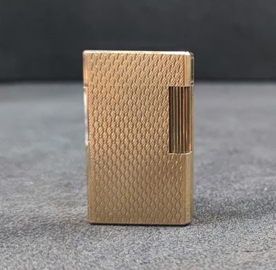 a gold lighter sitting on top of a table next to a black wall