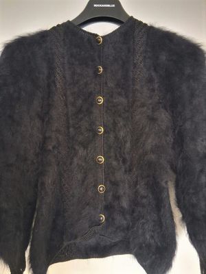 La veste est en fourrure de mouton noire et comporte des boutons sur le devant.
