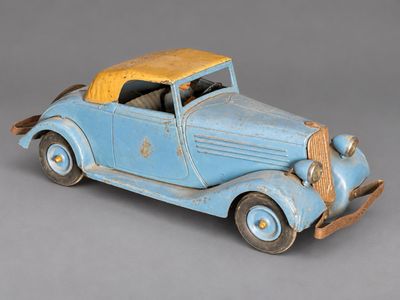 an old blue toy car with a yellow top sitting on a gray surface