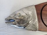 a metal fish head on a wooden plaque on a table