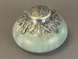 a small green vase with a silver lid on a table