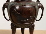 a bronze vase sitting on a wooden stand on a table
