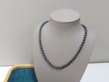 collier de perles grises présenté sur un plateau bleu avec un fond blanc