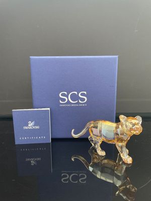 une figurine en verre représentant un lion, posée sur une table à côté d'une boîte bleue