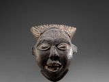 a close up of a wooden mask on a stand on a gray surface
