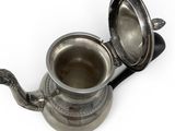 a silver tea pot with a handle on a white surface