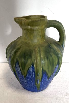un vase vert et bleu posé sur une surface blanche