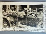 une vieille photo montrant deux hommes assis dans une voiture, avec un chien sur le siège passager
