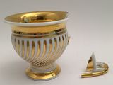 a gold and white vase next to a small gold object