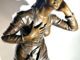 a bronze statue of a woman holding her hand to her ear