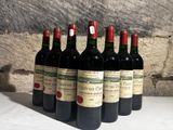 six bouteilles de vin rouge alignées sur une table devant un mur de pierre