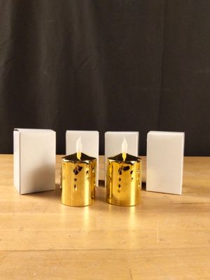 trois bougies dorées posées sur une table en bois, à côté d'une boîte blanche