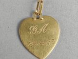 a close up of a gold heart charm with the initials of two people