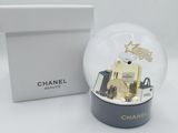 un flacon de parfum Chanel dans une boule à neige, à côté d'une boîte