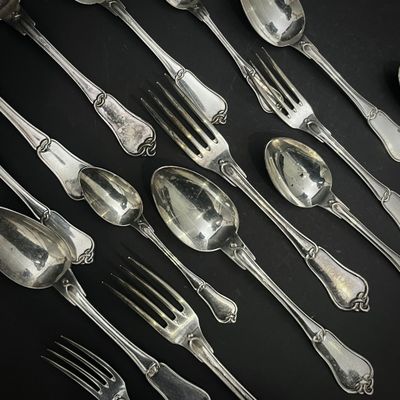 de nombreuses cuillères et fourchettes en argent posées sur une table noire