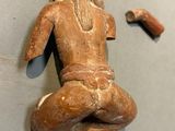 une statue en bois représentant une femme assise sur une table, à côté d'un morceau de bois