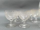 six wine glasses and a pitcher sitting on a table
