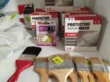 five paint brushes on a counter next to a box of protective masks