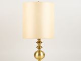 une lampe de table dorée avec un abat-jour beige sur fond blanc