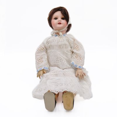 doll sitting on a white surface wearing a white dress and brown shoes
