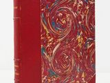 an old book with a red cover sitting on top of a white table