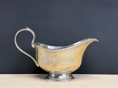 an antique silver plated gravy with a curved handle on a wooden table