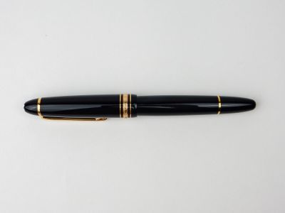un stylo plume noir et doré posé sur une surface blanche
