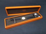 une boîte orange contenant une montre, posée sur une surface noire