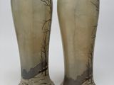 pair of vases with a landscape painted on them sitting on a white surface
