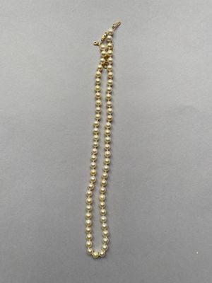 un gros plan d'un collier de perles dorées posé sur une surface grise