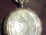 une montre de poche en argent posée sur un tissu rouge