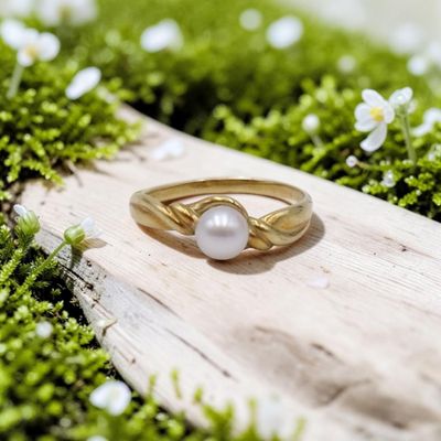 un gros plan d'une bague en or sertie d'une perle, posée sur une surface recouverte de mousse