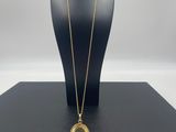 a gold plated necklace with a glass pendant on a black display stand