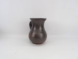 un petit vase brun posé sur une surface blanche