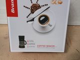 une boîte contenant une cafetière et un mot, posée par terre