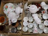 de nombreuses tasses et théières dans une boîte posée par terre